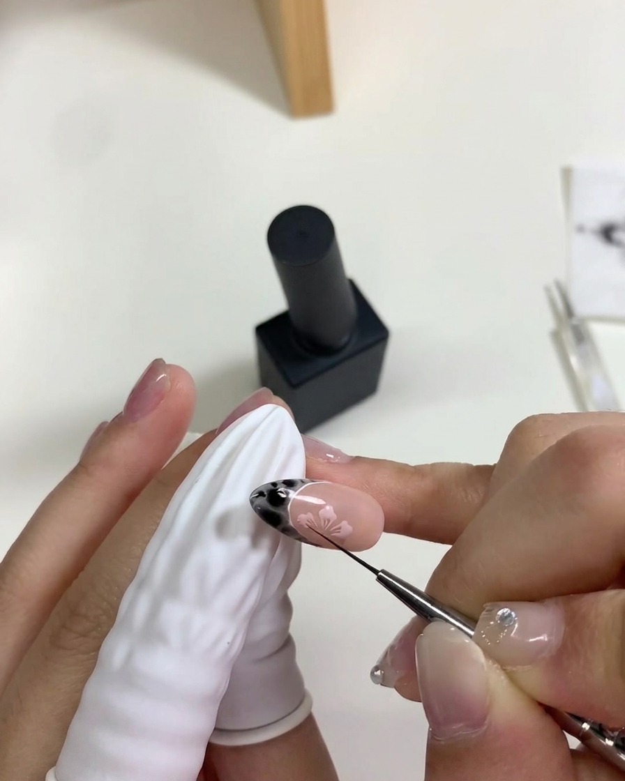A hand placing a nail under a portable mini UV/LED lamp to cure the pink gel cherry blossom art.