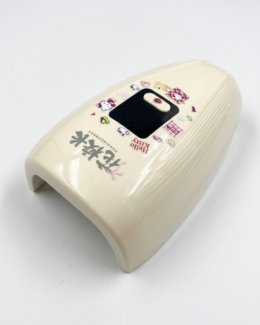 A cream-colored mini UV/LED nail curing lamp decorated with Hello Kitty stickers sitting on a bright white surface.