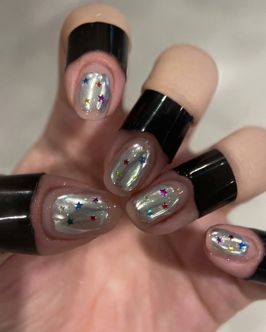 A dotting tool placing colorful star sequins onto the builder gel on a nail.