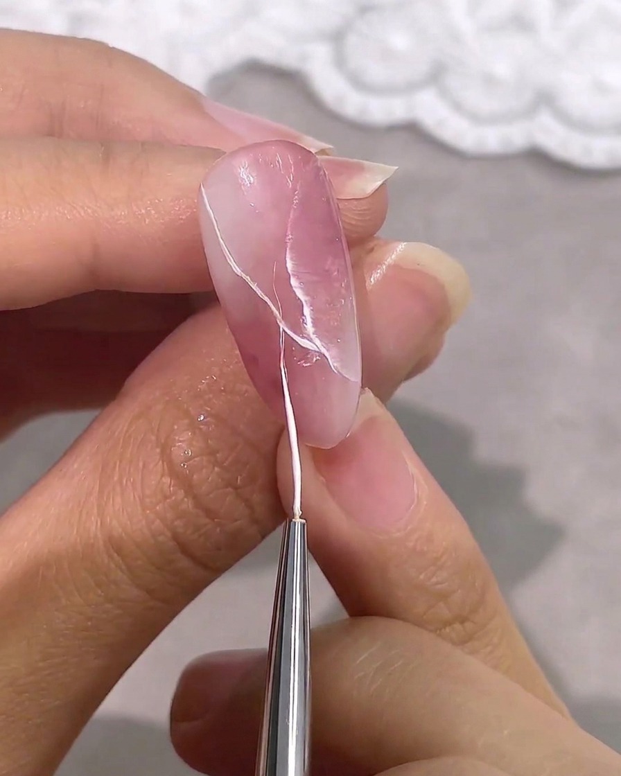 A fine liner brush adding thin, crisp white veins to a pink and white marbled nail design.