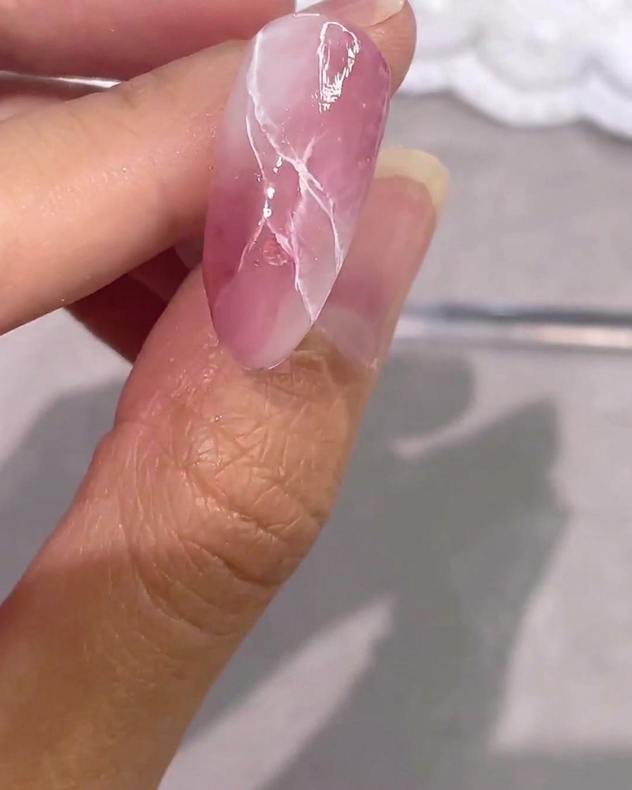 A completely finished pink marble gel nail with silver accents and a high-gloss top coat.