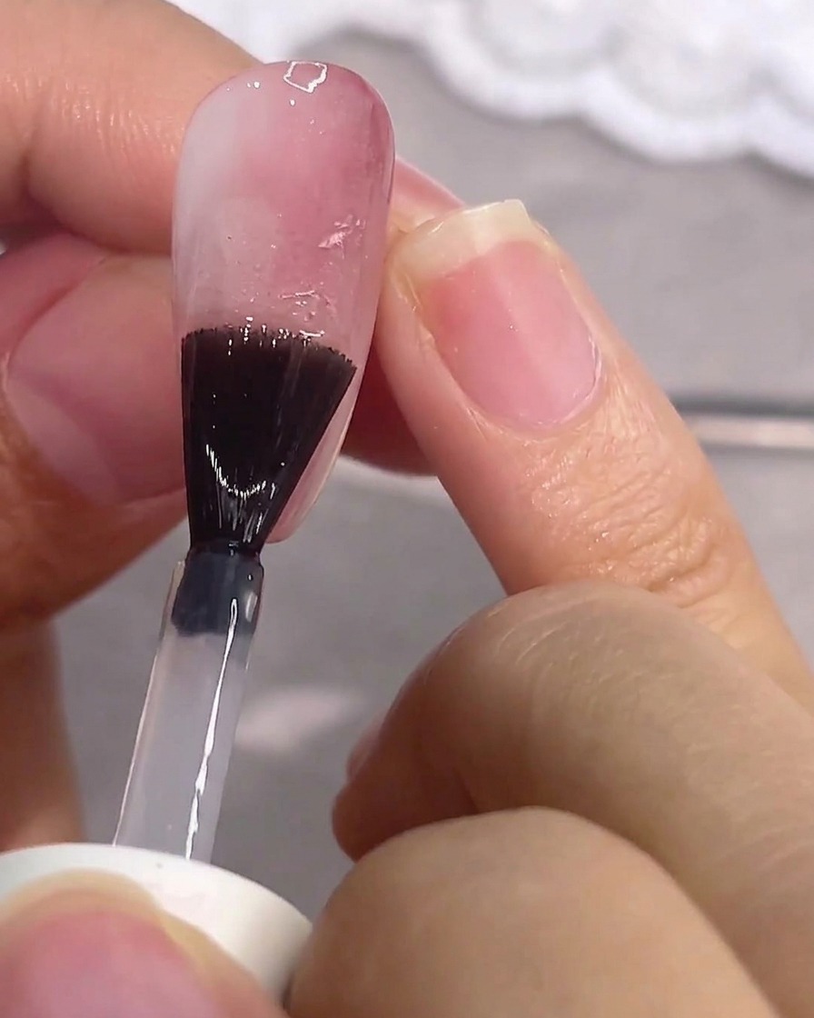 A brush applying clear matte top coat to a pink gel nail.