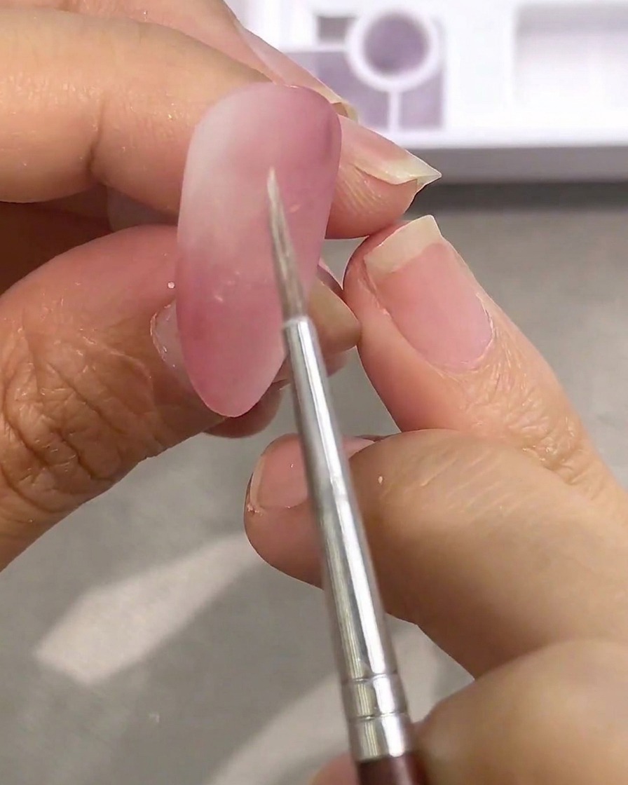 A close-up view of a fine detail brush being dipped into white watercolor paint on a palette.