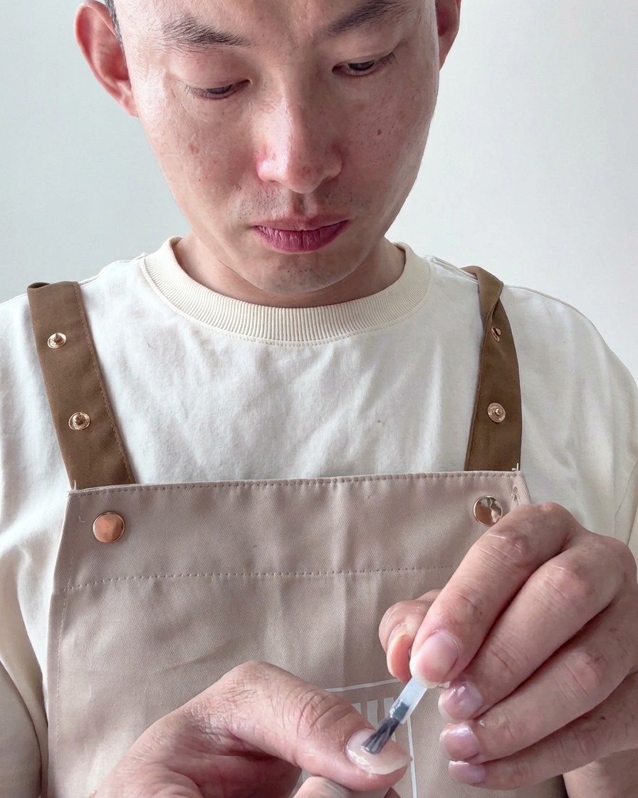 A nail brush applying a sheer, milky white gel polish to a prepared nail tip.