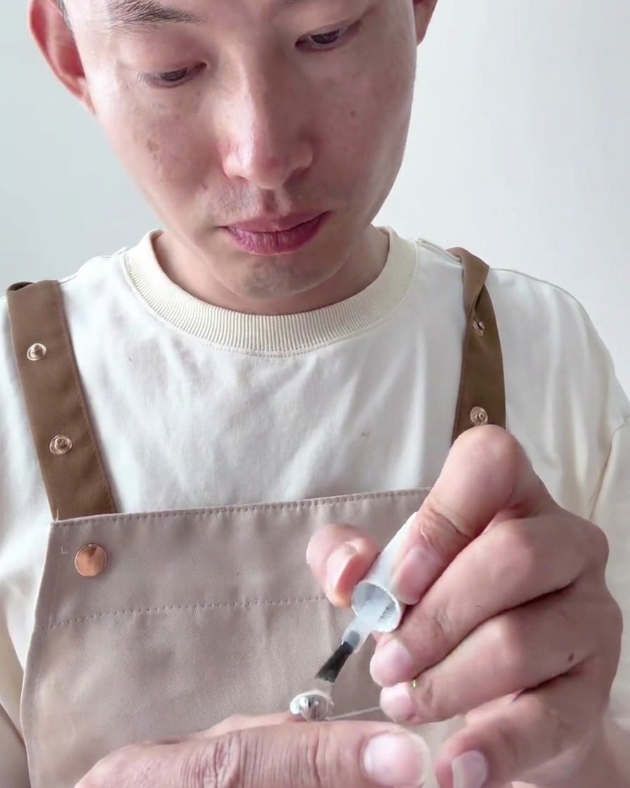 A close-up of a brush applying a second coat of opaque milky white gel polish onto the nail tip.