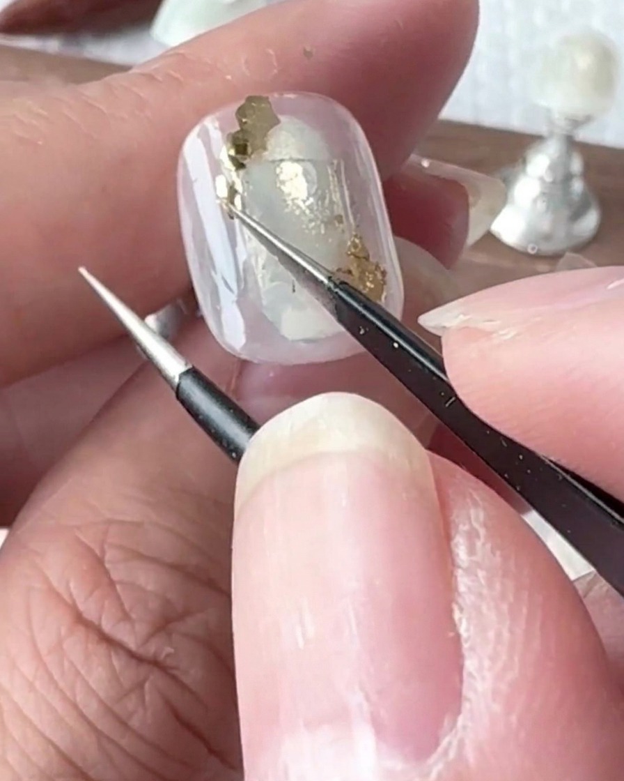 A small detail brush applying tiny drops of clear gel onto the surface of a painted nail.