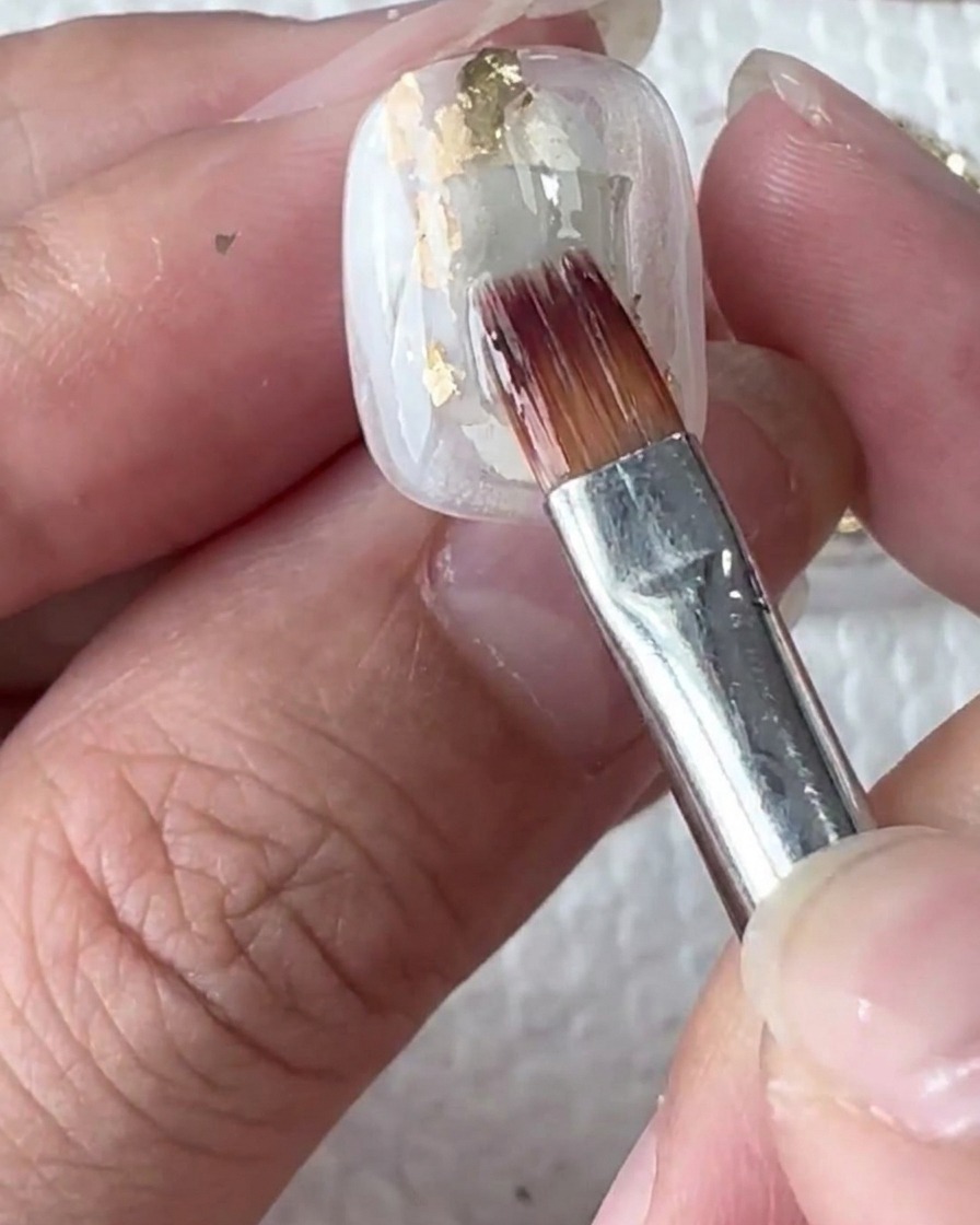 White gel drops sitting on the wet surface of the nail.