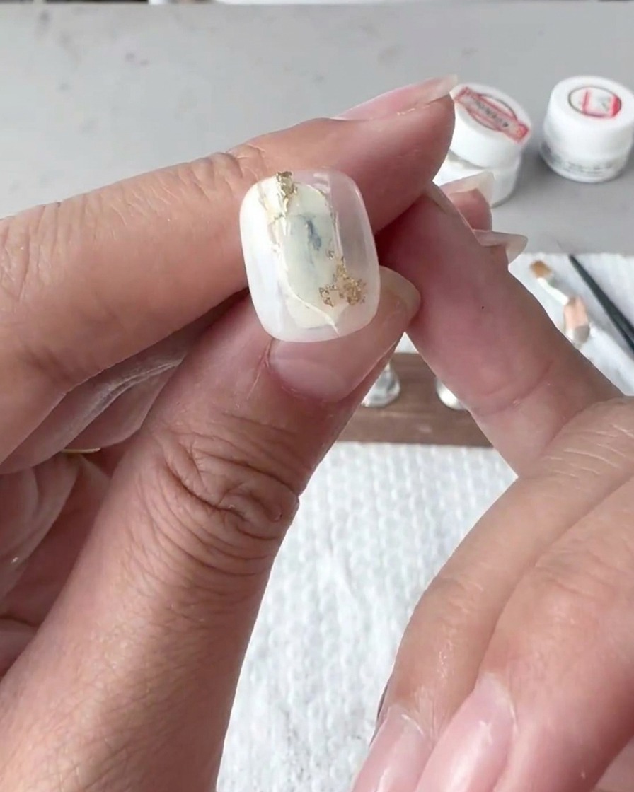Close-up of a flat brush delicately blending and blurring white gel polish lines on a nail tip.