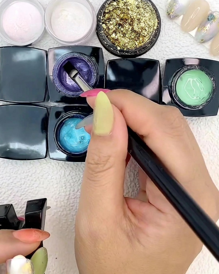 A flat nail art brush applying blue gel onto a nail tip.