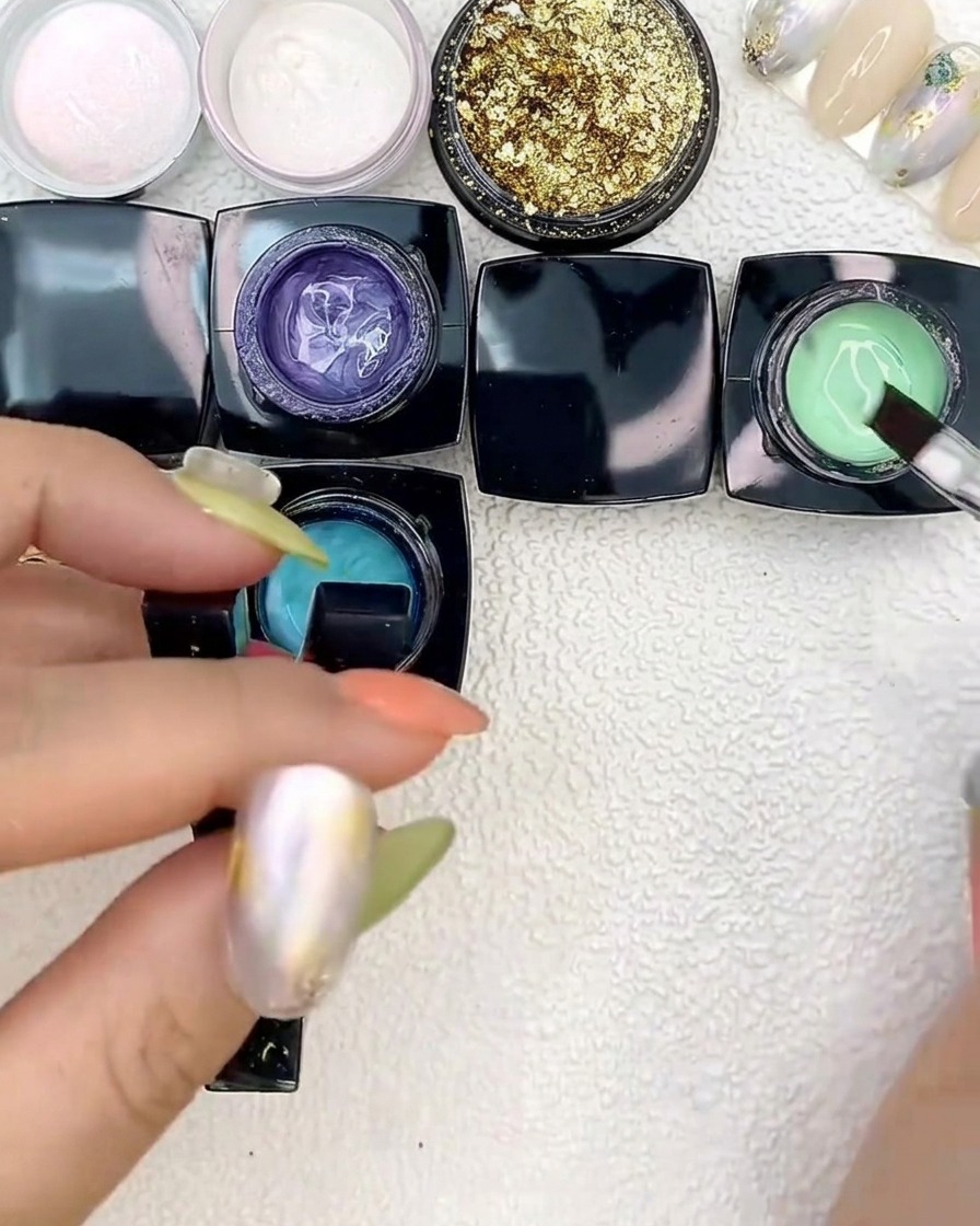 Applying bright green gel next to blue patches on a nail tip using a flat brush.