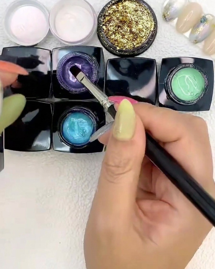 A brush placing purple gel alongside blue and green gels on a nail.