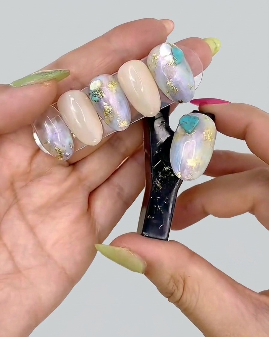 A pair of tweezers placing small, delicate pieces of gold leaf onto a decorated gel nail.