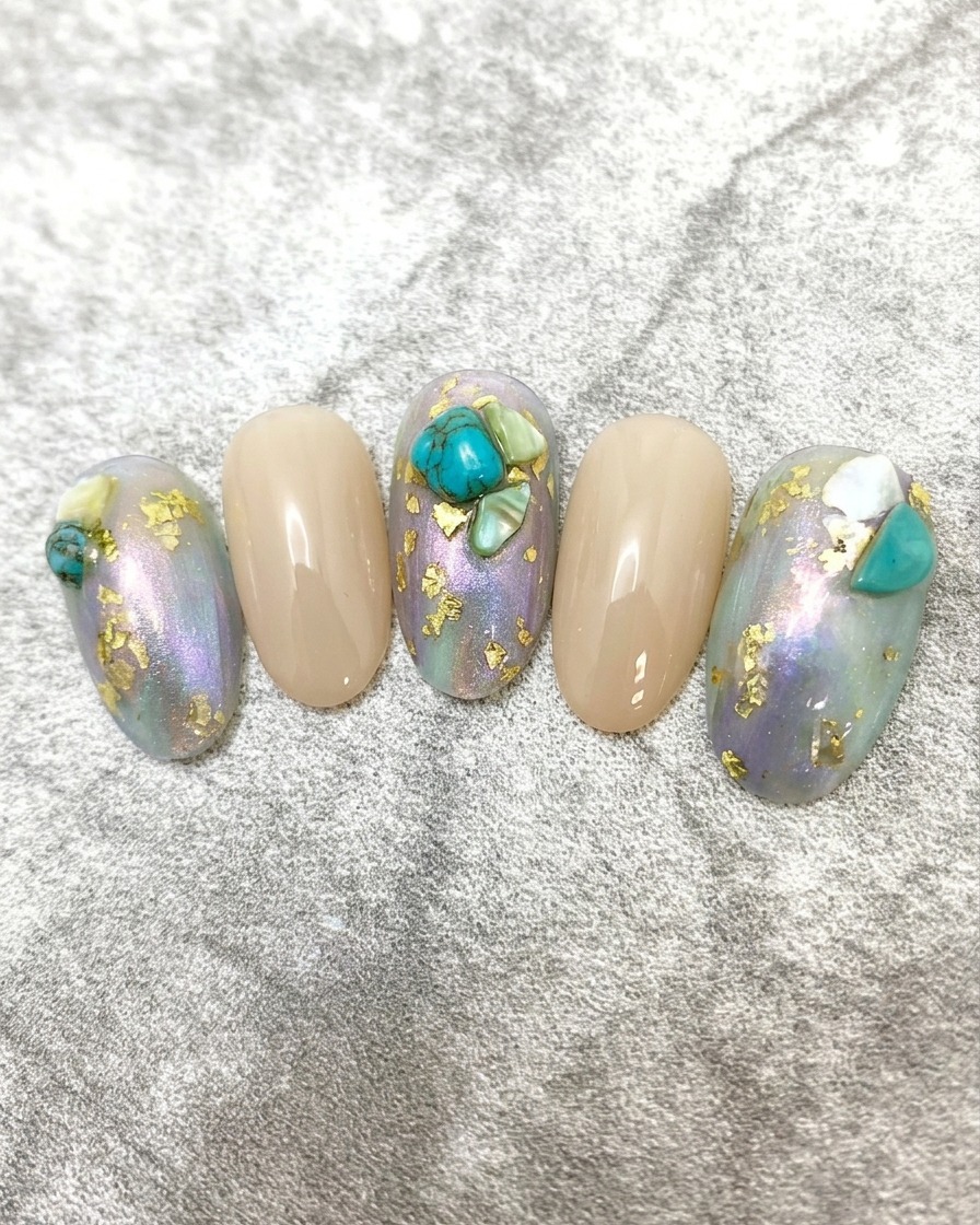 A close-up showing a small, vibrant turquoise stone being positioned onto a nail surface with a detail brush.