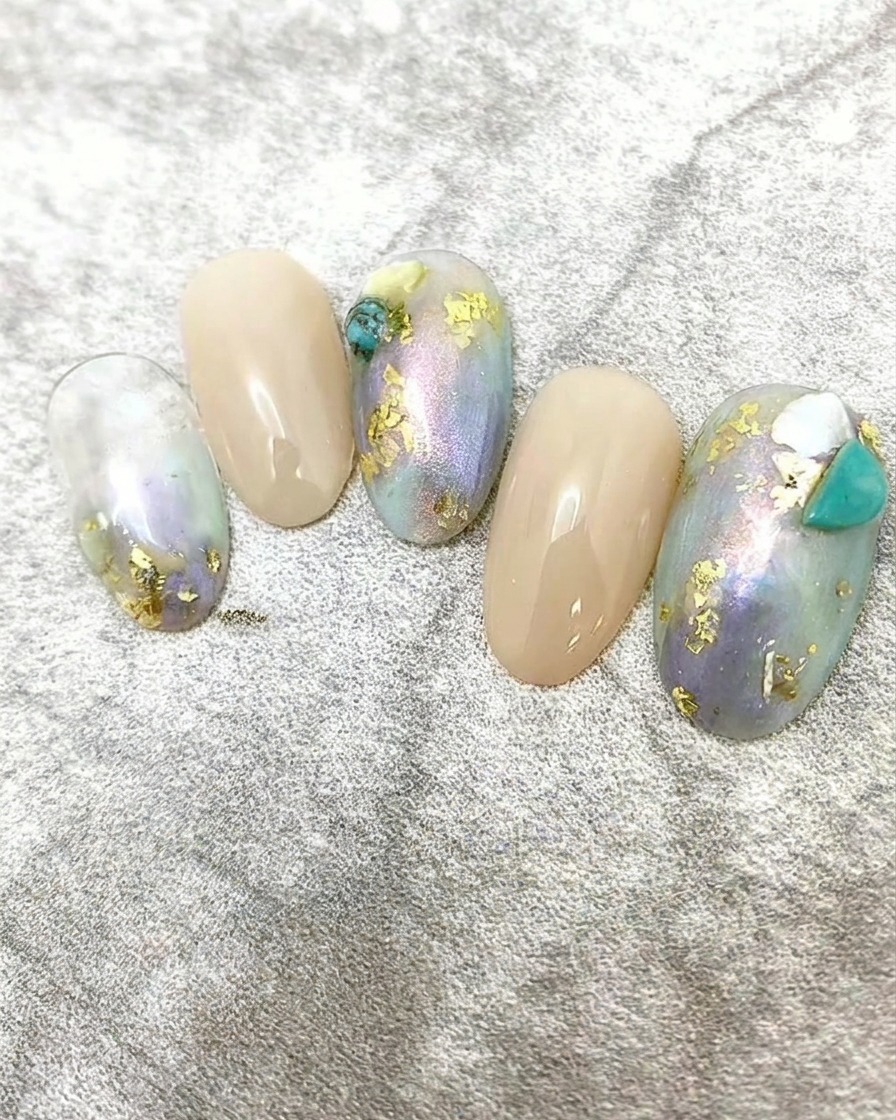 Tiny pieces of white shell flake being applied to a nail design as accent decoration.