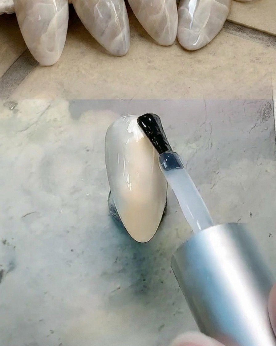 A brush applying a layer of clear gel over the nail surface to prepare for blending.