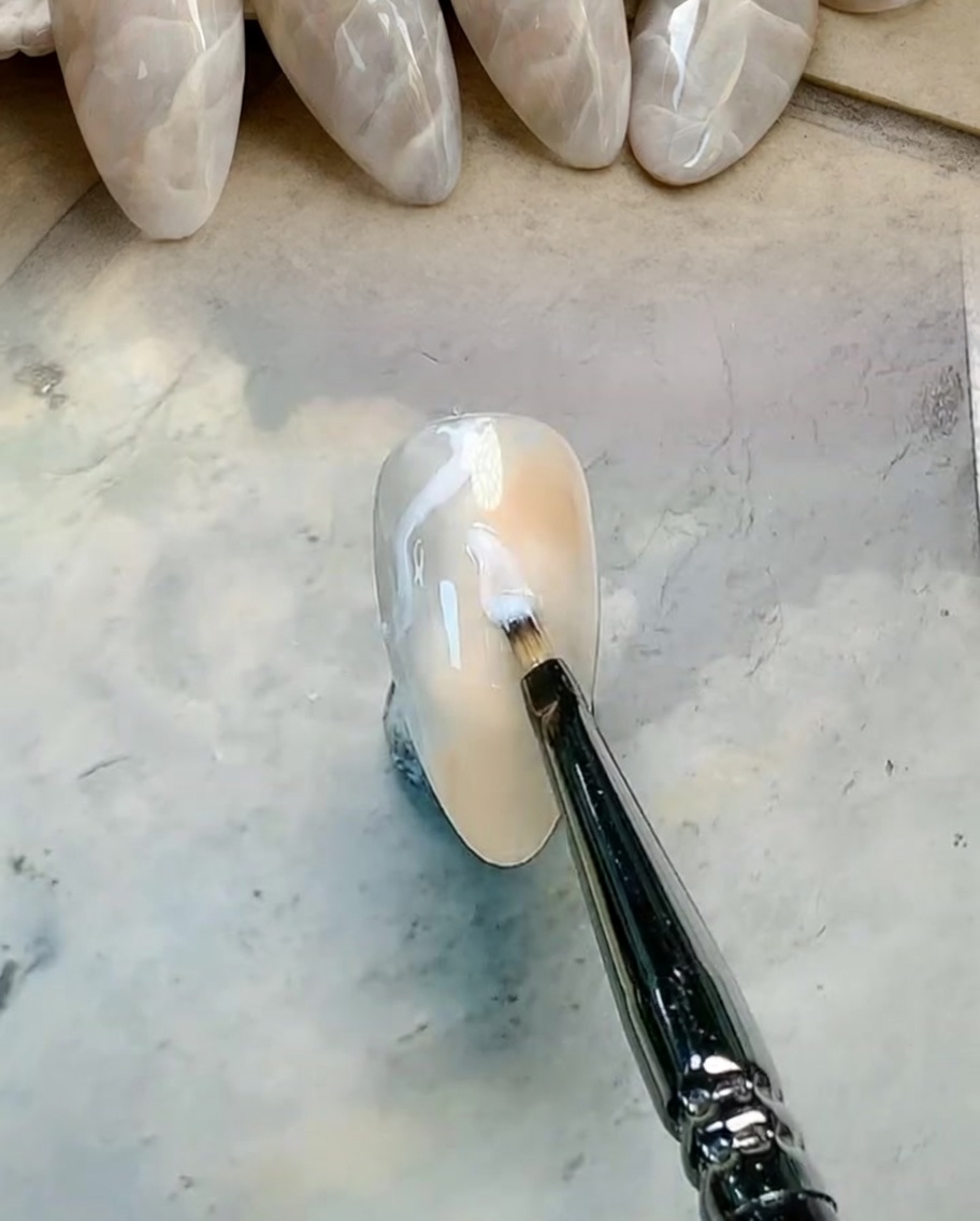 A flat brush blending brown and gray gel colors on the nail to create a soft gradient.
