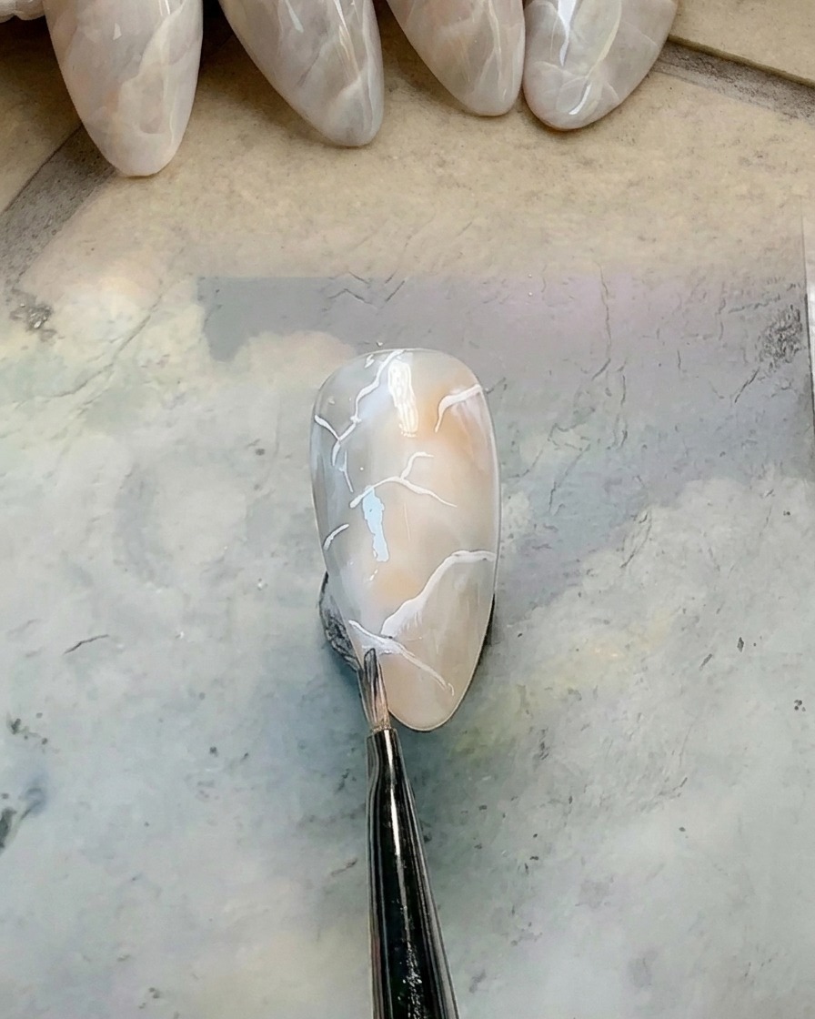 A small clean round brush blurring the edge of a white gel line on a marbled nail.
