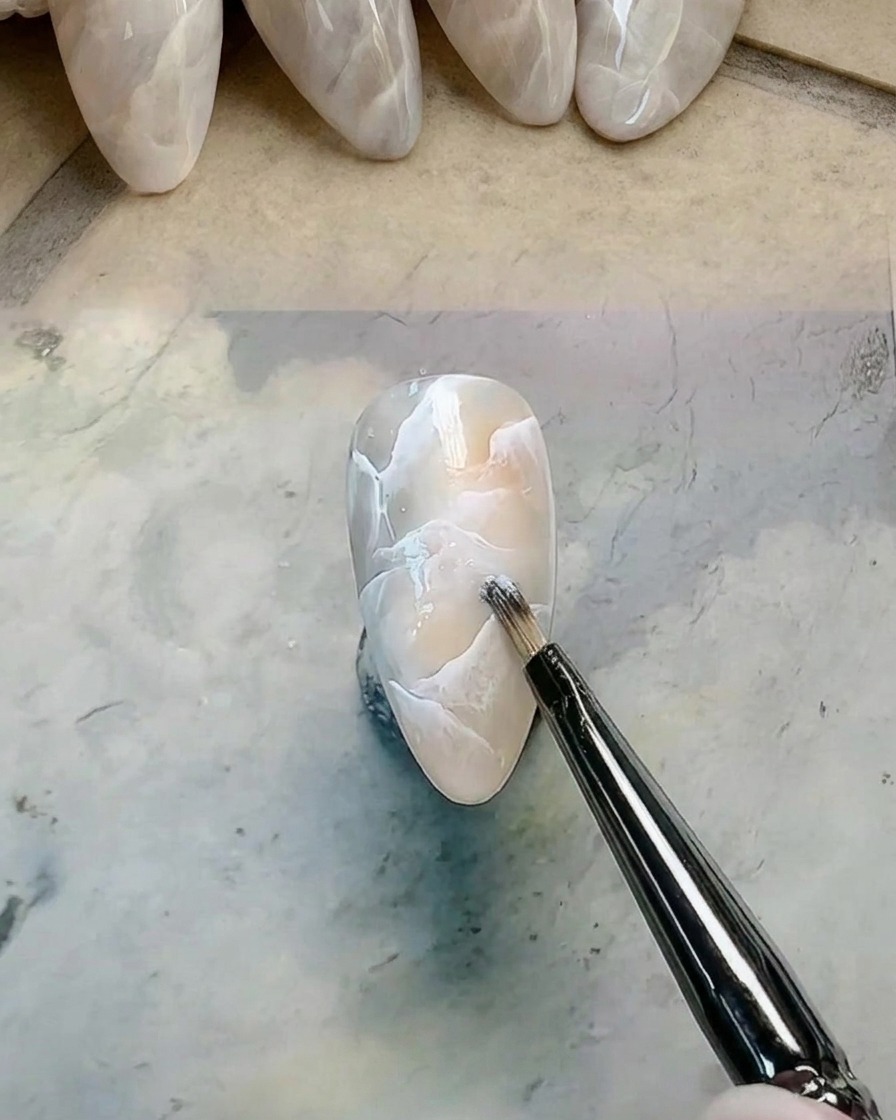 A detail brush adding and smudging extra white gel onto a marbled nail design.