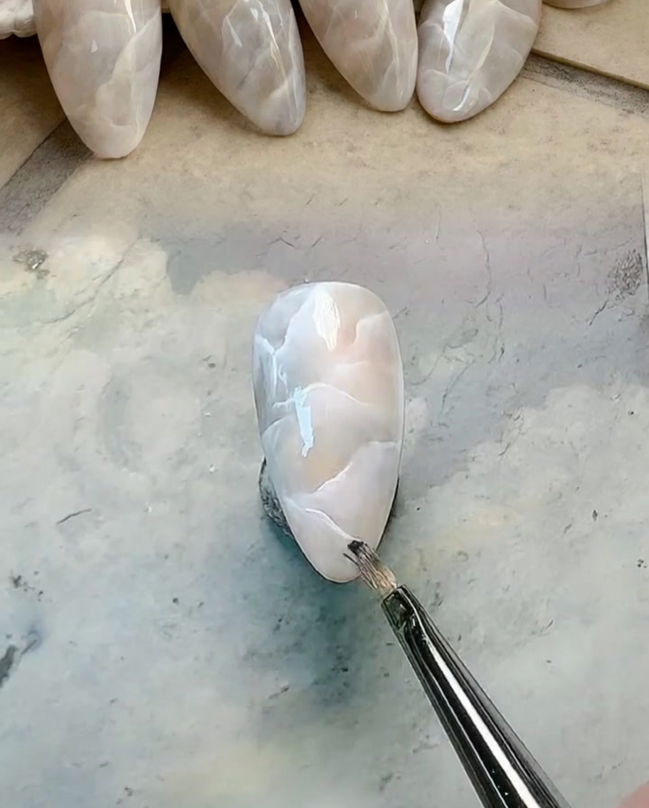 A fine liner brush drawing crisp white veins on top of a milky marbled nail design.