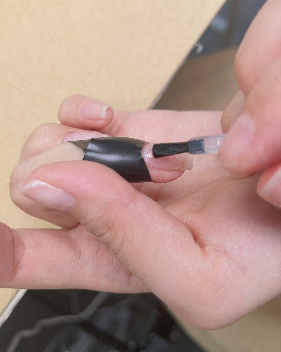 A brush applying a clear, glossy layer of blooming gel over a nude base.
