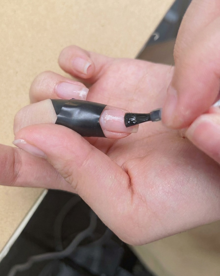 A fine detail brush applying a dot of vibrant pink polish to the center of a nail covered in wet blooming gel.