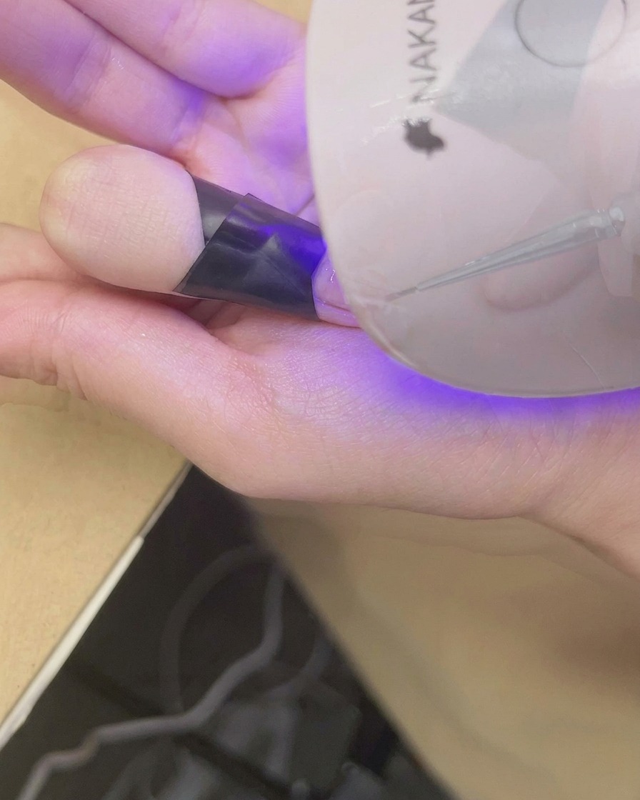 A finger placed under a mini UV/LED lamp to cure the finished blush gradient nail art.