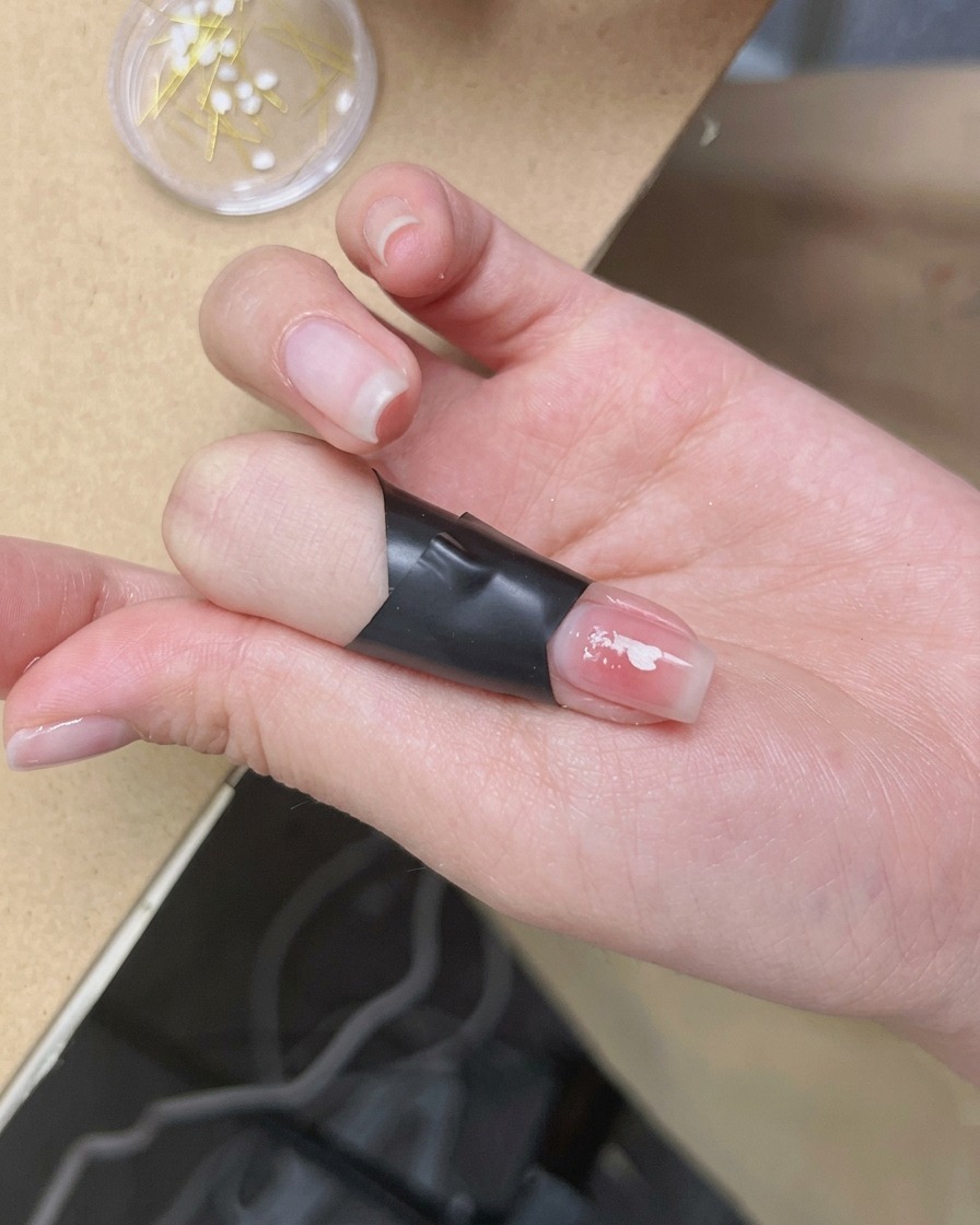 A pair of tweezers placing a delicate white cherry blossom ornament onto the center of a manicured fingernail.
