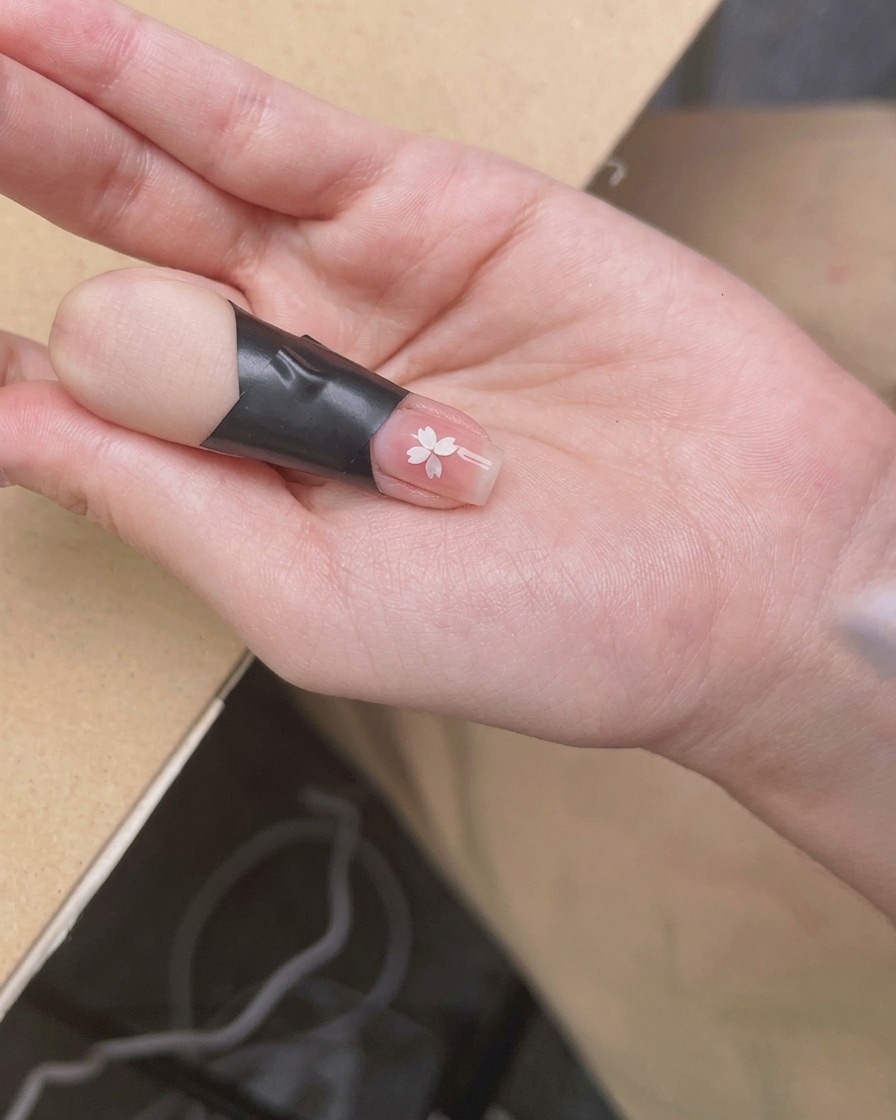 A hand positioned under a compact UV/LED nail lamp, with the focus on the nails receiving the light.