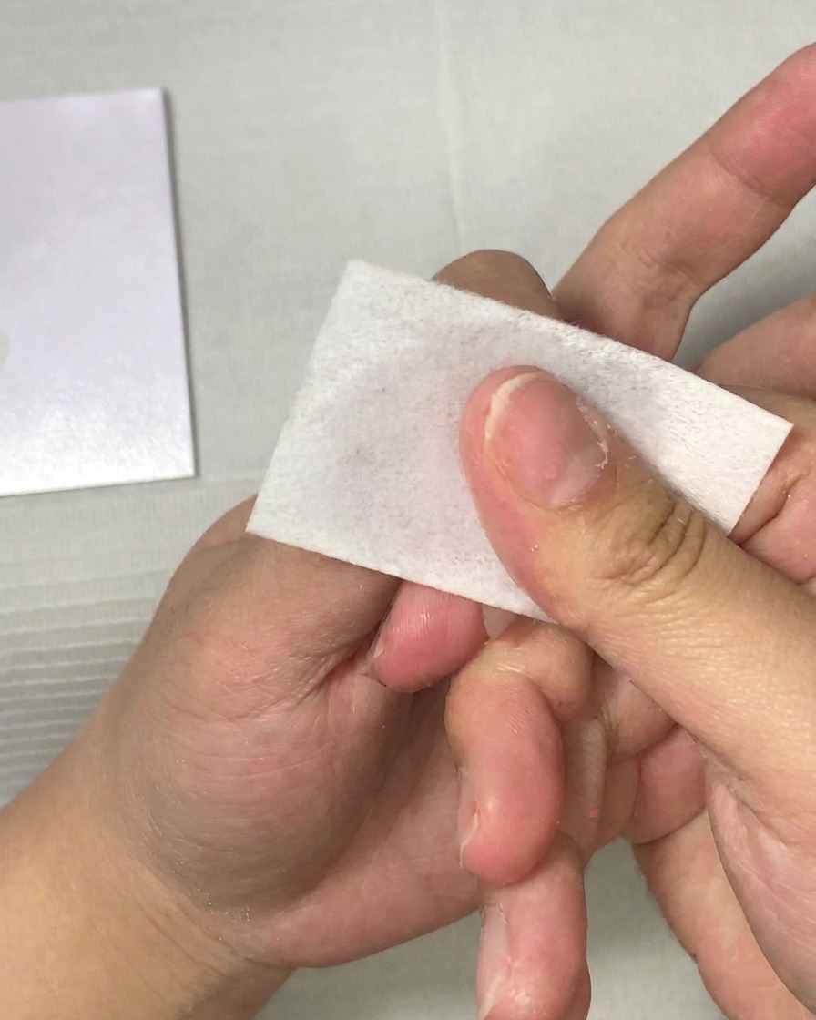 A close-up of a hand using a lint-free wipe to clean a fingernail.