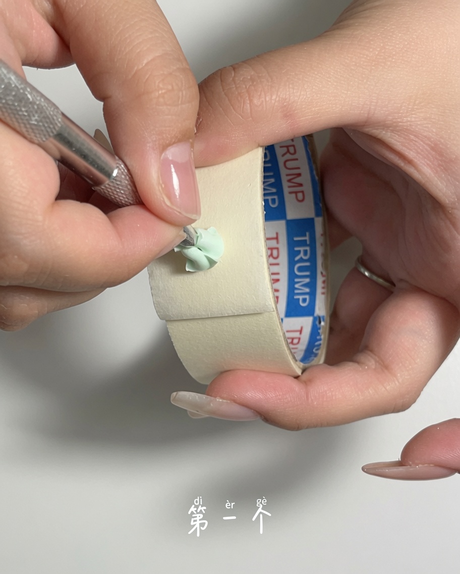 A metal cuticle pusher being used to gently scrape dust off the surface of a green makeup sponge.