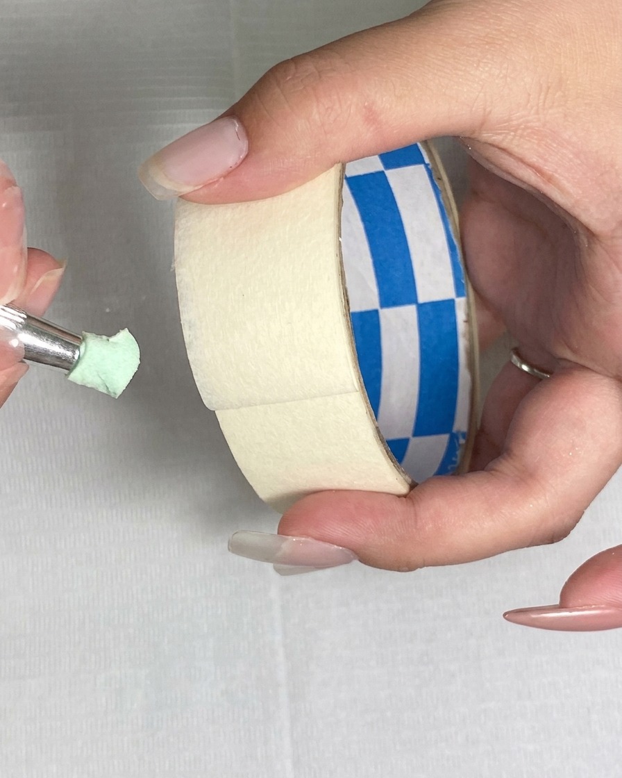 Using a piece of masking tape to lift fine particles from the surface of a green sponge.