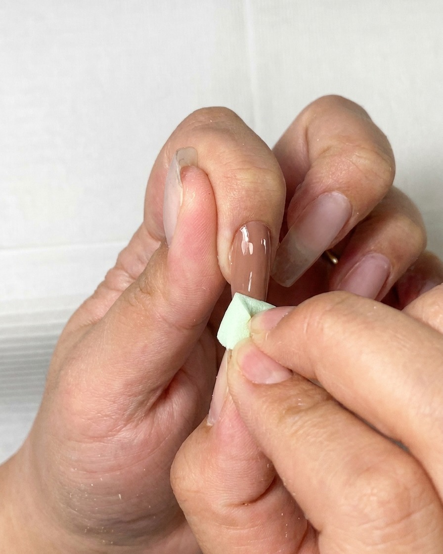 A brush applying a smooth coat of brown gel polish onto a natural nail.