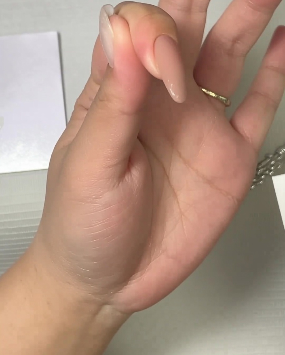 A brush applying a matte top coat to a neutral-toned nail.