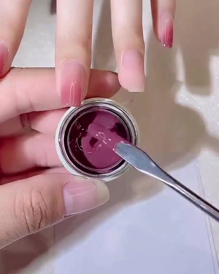 A metal mixing stick lifting a small dollop of purple-pink jelly gel out of a small jar.