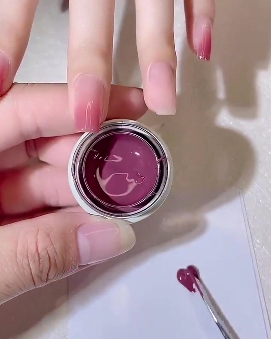 A metal tool spreading a small amount of purple-pink gel thinly across a white palette paper.