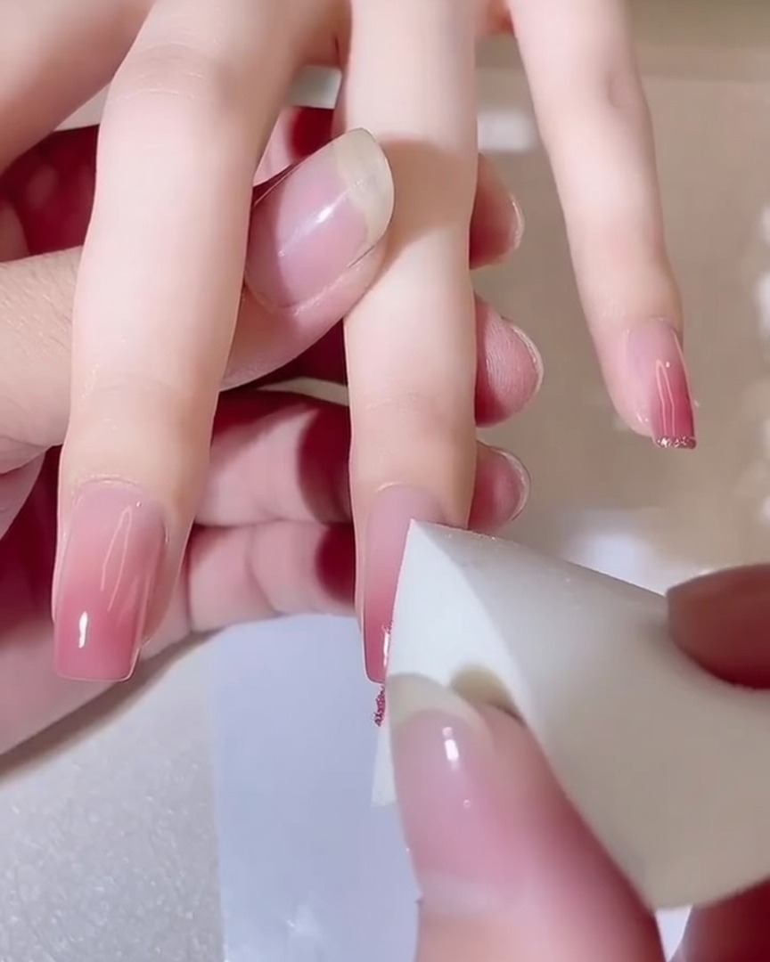 Close-up of a sponge dabbing onto a fingernail, showing a deepening pink gradient effect.