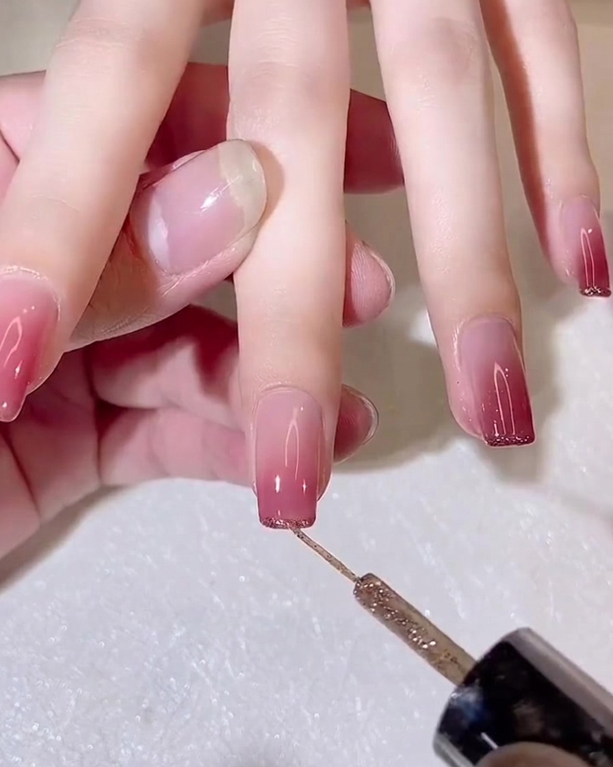 A fine-liner brush applying a thin line of gold glitter gel to the free edge of a gradient nail.