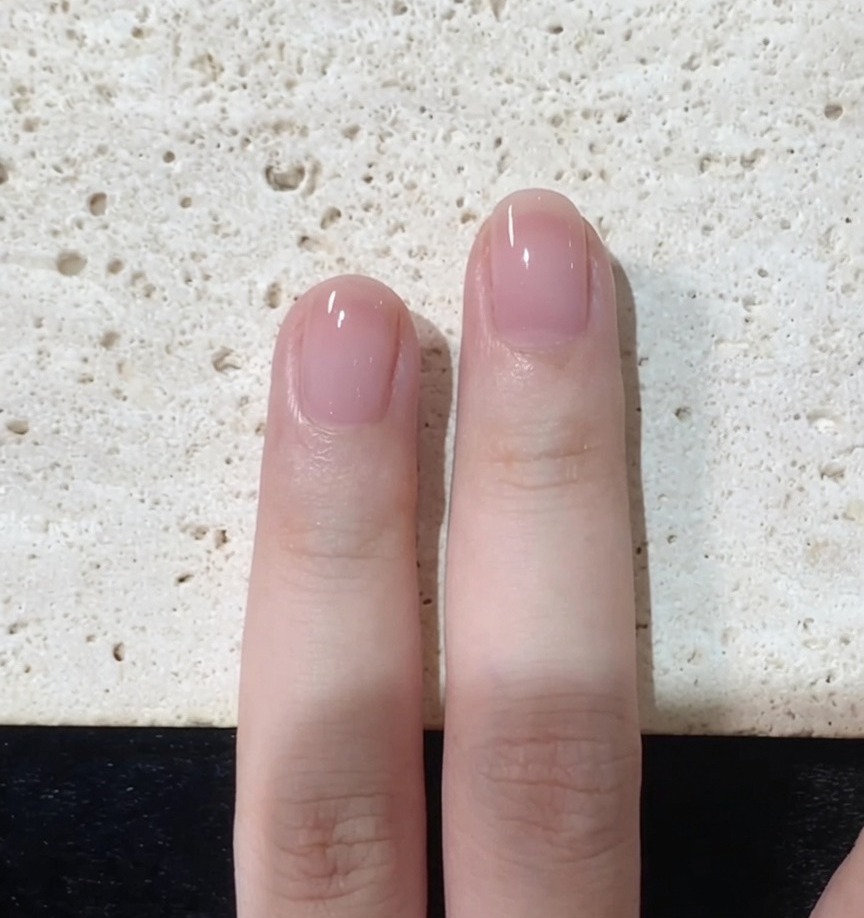 A nail brush carefully refining the edges and tip of a pink-painted fingernail.