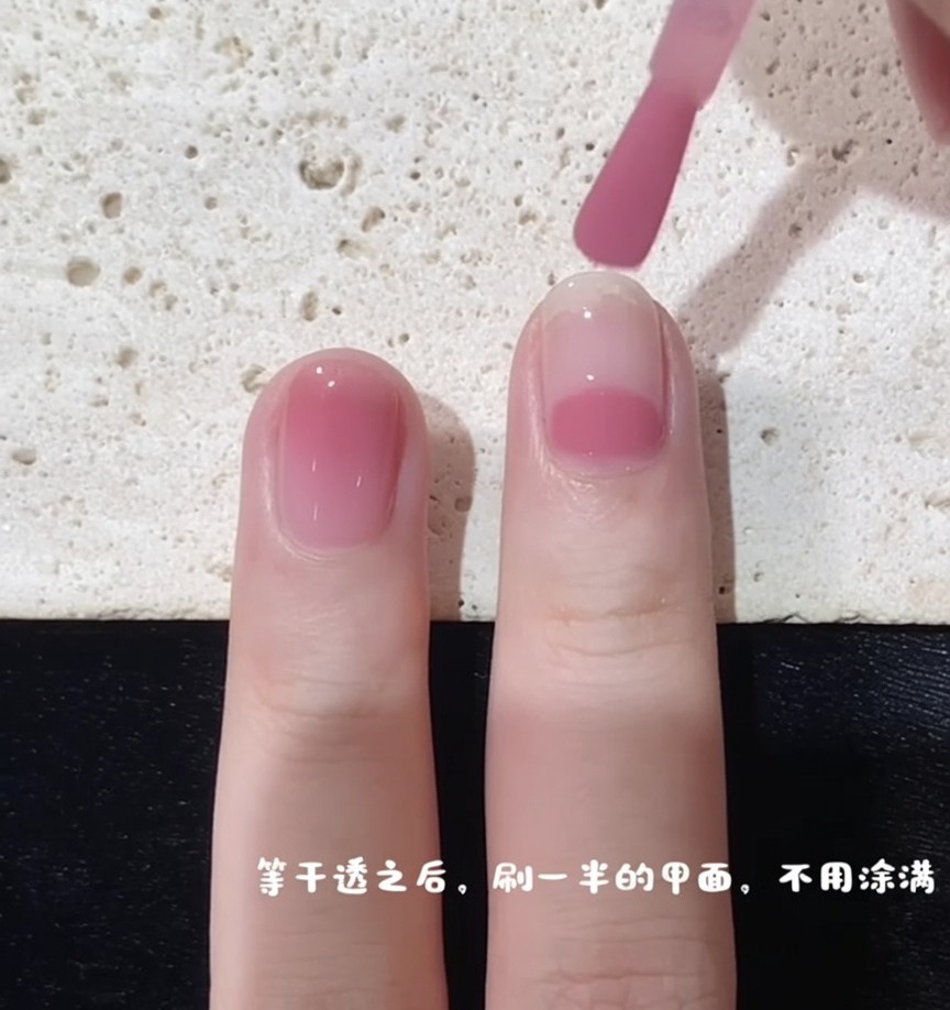 A nail brush starting an application of pink polish at the midpoint of the nail to create a gradient effect.