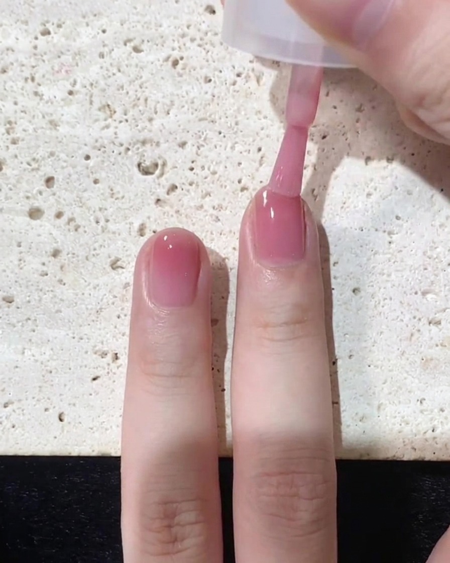 A nail brush applying a final concentrated layer of pink polish specifically to the very tip of the nail.