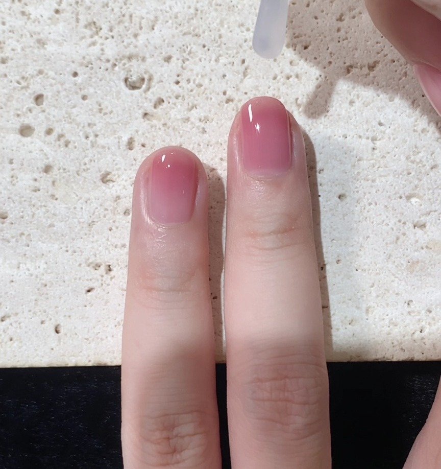 A brush applying a clear, glossy top coat over the completed gradient nail look.