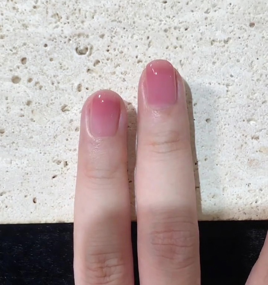 A close-up view of the final top coat application being smoothed over a pink gradient nail.