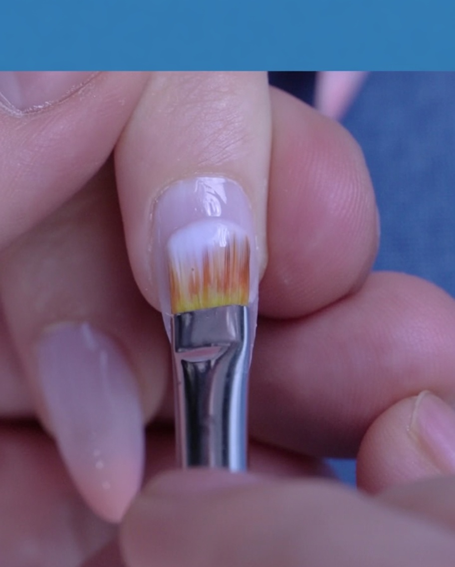A brush applying a translucent, milky white gel polish over a natural nail.