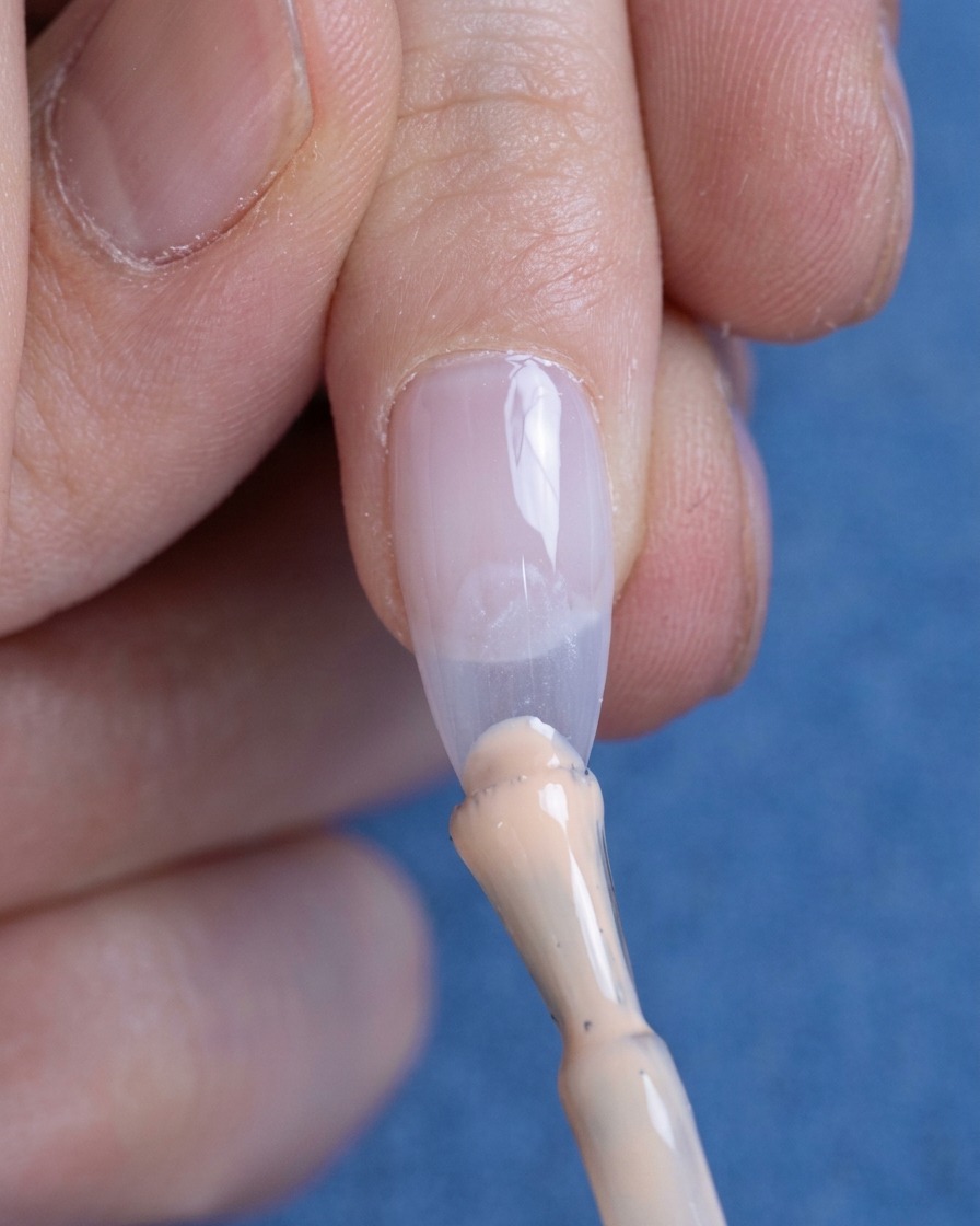 A small bead of nude gel polish being applied to the tip of a nail.