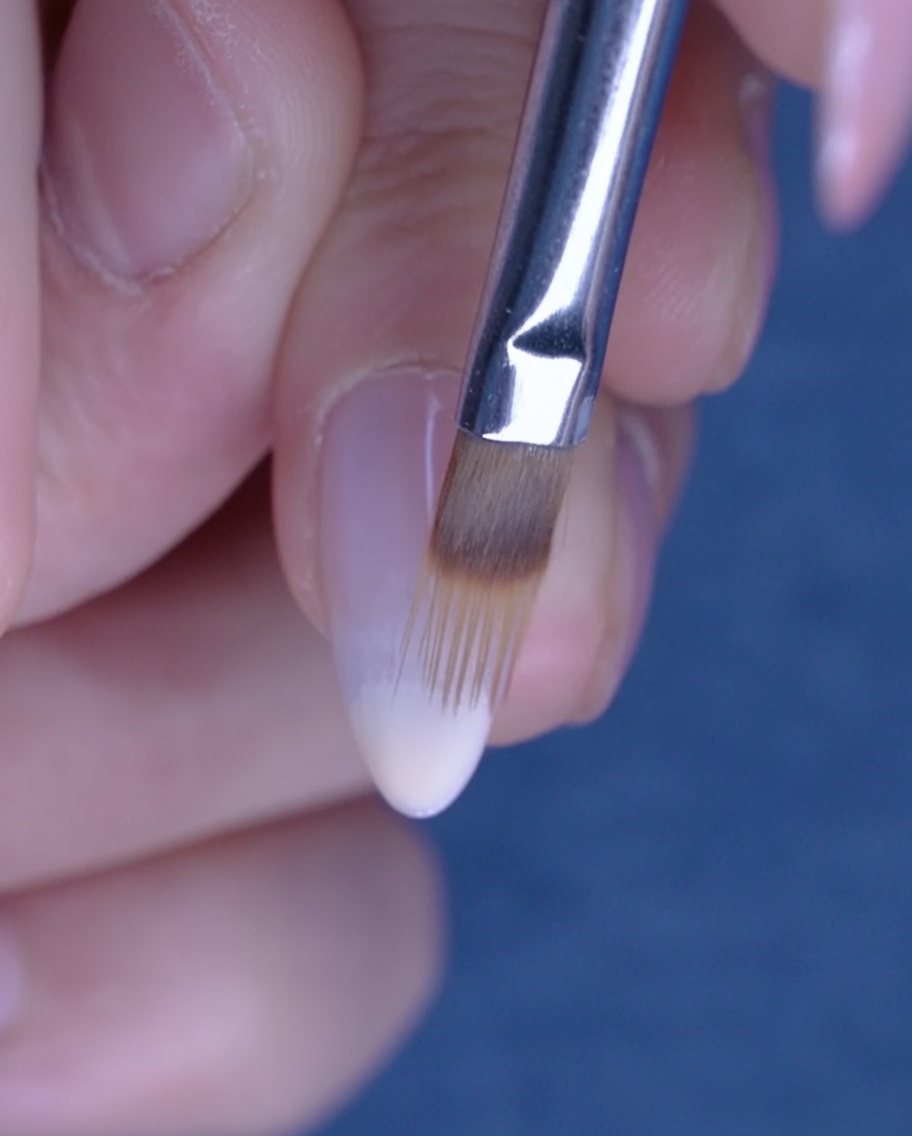 A flat brush blending nude gel polish upward on the nail to create an ombre effect.