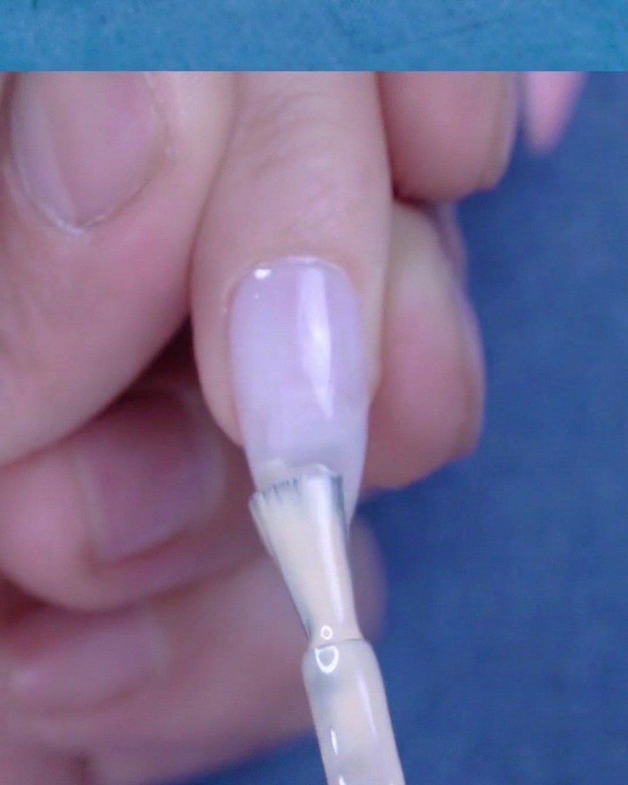 Applying a second, more concentrated layer of nude gel polish to the nail tip.