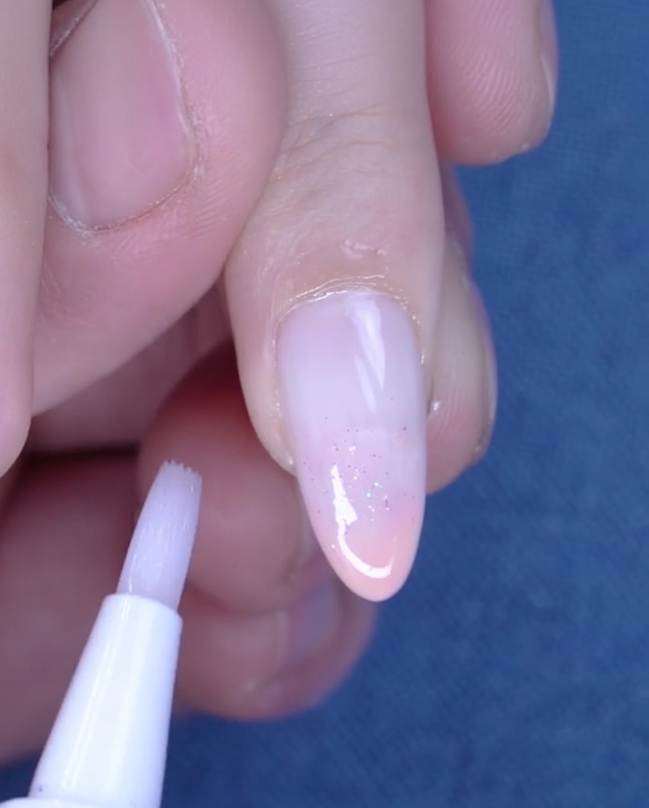 A cuticle oil pen being used to apply oil to the hydrated skin around a freshly manicured nail.