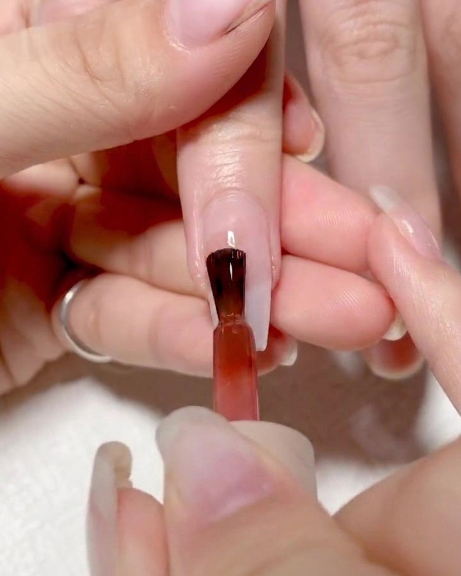 A nail brush applying vibrant red gel to the left side of a nail.