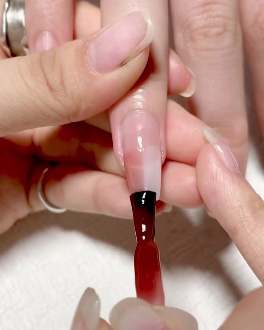 A specialized gradient brush dabbing the center of the nail where the red and clear gel meet to soften the line.