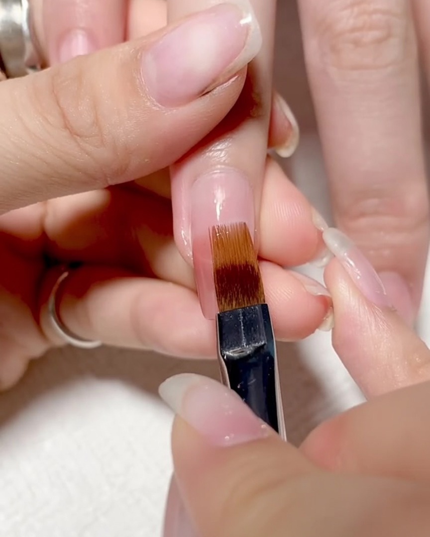 A brush being pulled gently downwards over the nail surface to blend the colors into a smooth ombre.